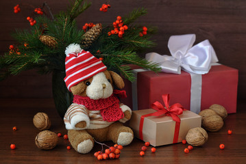 Little toy puppy in a knitted hat and a Christmas tree branch. Nuts and some gifts on an old wooden background