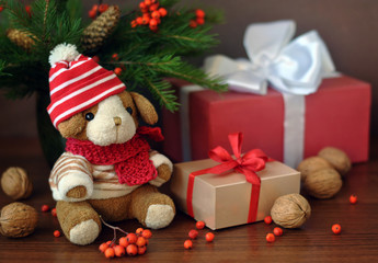 Little toy puppy in a knitted hat and a Christmas tree branch. Nuts and some gifts on an old wooden background