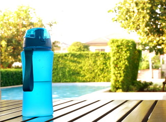 Obraz premium Blue bottle of drinking water on wood table at pool with natural background