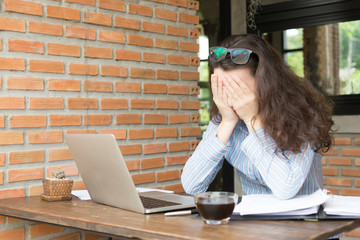 unhappy young woman working with her laptop.Female office worker Use her hands to cover her face...