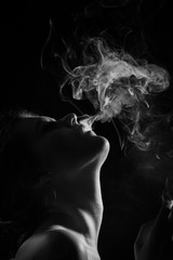 young woman with clouds of smoke smoking on black background, monochrome