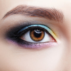 Closeup macro shot of human female eye. Girl with perfect skin and lilac - blue - yellow eyes shadows