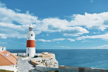Fototapeta na wymiar A view of beautiful red and white Trinity Lighthouse, orange tile roofs and vivid blue water at Europa Point at Gibraltar, the meeting point of Mediterranean Sea and Atlantic Ocean, United Kingdom.