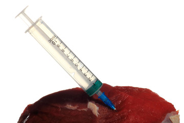 Syringe in a pork meat. White isolated background.
