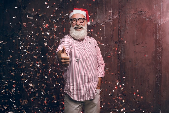 Happy bearded and modern man in Santa's hat and in fashionable glasses shows agree good gesture fingers up and happy smile in gold confetti. Happy New Year 2018 and modern party with fashion Santa
