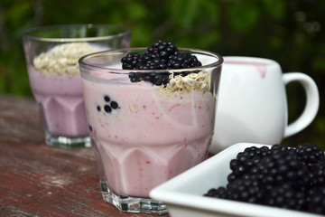 Overnight oats with blackberry yogurt. Delicious breakfast in glass cups on old wooden table, outdoor background,
