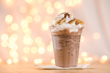 Banana cocoa in a plastic beaker to take out. Chocolate banana smoothie in glass with paper straw on wooden background, selective focus, horizontal, toned