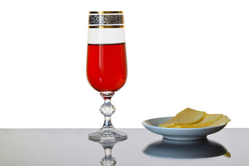 A wineglass of pink wine and a plate with pieces of cheese on a mirror background.