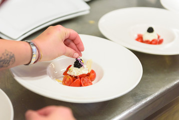 Preparation of appetizer with small tomatoes. white ball and a blackberry on white plates