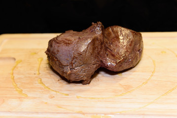 Cooked meat fillet on a wooden board, black background