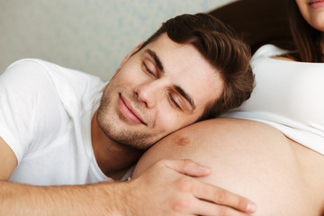 Fototapeta na wymiar Happy young husband lying on his pregnant wifes belly