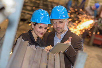 Manager giving technical instructions at a woman worker on a digital tablet in a steel factory