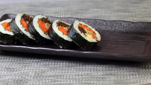 Woman hand putting pieces of korean dish Gimbap or Kimbap with tuna and vegetables on ceramic plate
