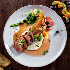 Delicious medium rare meat steak with sauce and salad on a plate. Healthy food made of meat fillet and fresh herbs on a wooden table. Top view.