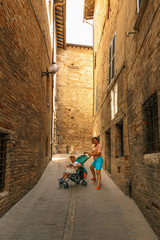 Fototapeta na wymiar A woman with a baby stroller in the narrow street of Italy.