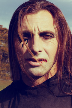 Portrait of man with long red hair and with Halloween make up in black costume  outdoor. Halloween or horror theme.
