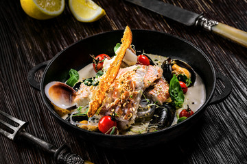 Delicious Asian meal made of sea bass fish, mussels, crab meat and other seafood with tomato and rice noodles on a rustic wooden table.