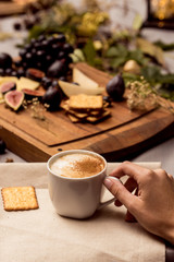 Hand holds cup of coffee with food in background