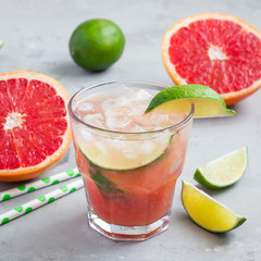 Cold pink cocktail with fresh grapefruit, lime and ice cubes on concrete background, paloma, square