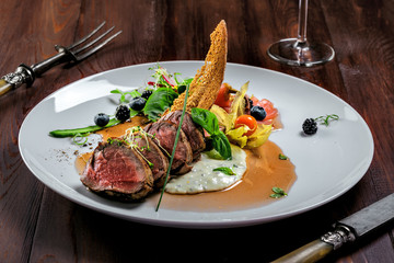 Delicious medium rare meat steak with sauce and salad on a plate. Healthy food made of meat fillet with fresh herbs and wine on a wooden table.