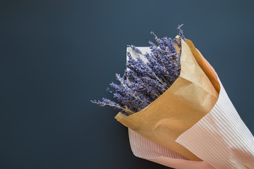 A bouquet of dry lavender in kraft paper on a dark background, symbolizing summer and France. Flat lay, top view.