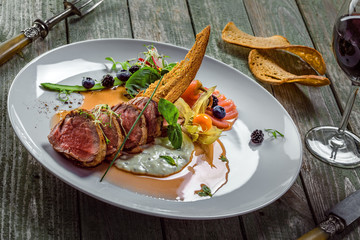 Plate with medium rare meat steak, sauce and salad on a wooden table. Healthy gourmet food made of meat fillet and fresh vegetables.