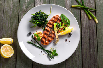 Salmon fish stake cooked on a grill with healthy salad on a plate. Healthy food made of fish and vegetables on a table. Top view.