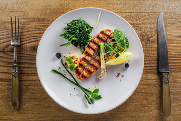 Gourmet grilled salmon fish steak and vegetable salad on a plate. Delicious healthy meal made of fish and vegetables on a rustic table. Top view.
