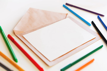 Blank sheet of paper on craft envelope. Background with colorful pens. May be used as mock up.
