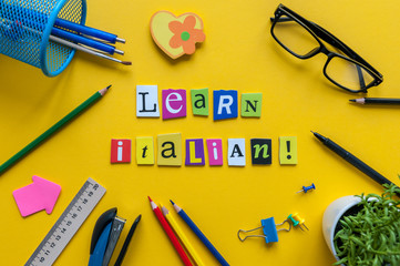 Word LEARN ITALIAN made with carved letters onyellow desk with office or school supplies,...