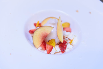 Close up of a ball of ice cream decorated with peach slices and orange petals on a white dish decorated with colorful pieces