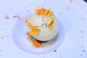 Close up of a ball of ice cream decorated with orange petals on a white dish decorated with colorful pieces