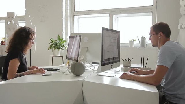 Two people are seriously working at desk in creative office window. Man and woman carefully typing in front of computer monitors on an important project.