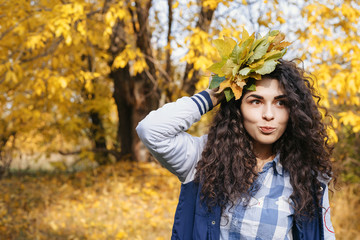 Happy curly woman holding bouquet of autumn leaves in hand and posing in autumn park.