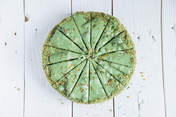 Pistachio cake sliced on white wooden background