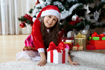 Celebration of Christmas, winter holidays and people concept. Happy young girl with gifts in boxes sitting near a decorated Christmas tree at home