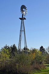 tall vintage farm  windmill in a rural Autumn landscape, blue sky background 