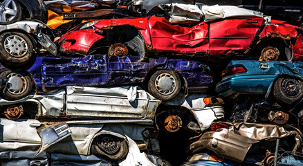 A close up of a stack of red, purple, blue and white compressed cars at a junkyard