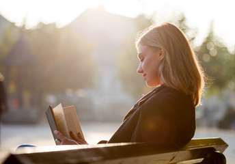 Young girl reading book at sunset on the city street