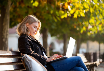 Woman using laptop in the city street under colorful autumn trees - obrazy, fototapety, plakaty