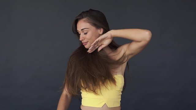 Woman in yellow top shakes her long brown hair and touches her face tender