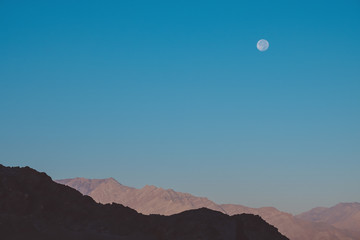 Landscape mountain image with the moon in clear blue sky background