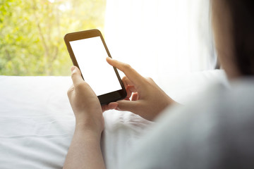 Woman using (holding) smartphone on bed in morning with window view.lifestyle activity concepts.