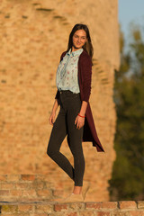 a beautiful girl poses in front of a medieval fortress at sunset