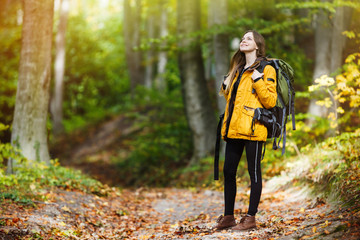Cheerful brunette tourist girl wears orange jacket and backpacked have walk through forest, autumn tourism concept