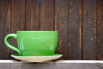 A big Green color coffee cup with dark wood panels copy space wall as background.