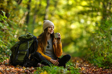 Beautiful brunette tourist girl wears cap and backpacked have break with cup of tea sitting in the...