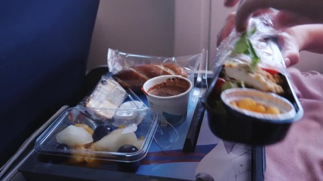 The woman unpacks her portion of food on the plane. In the frame are visible only hands