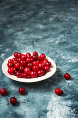 Fresh juicy cranberries on a white plate on a blue marble background with copy space