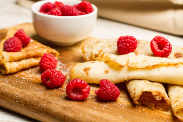 Crepes con frambuesas sobre tabla de madera rústica. Vista de frente y de cerca